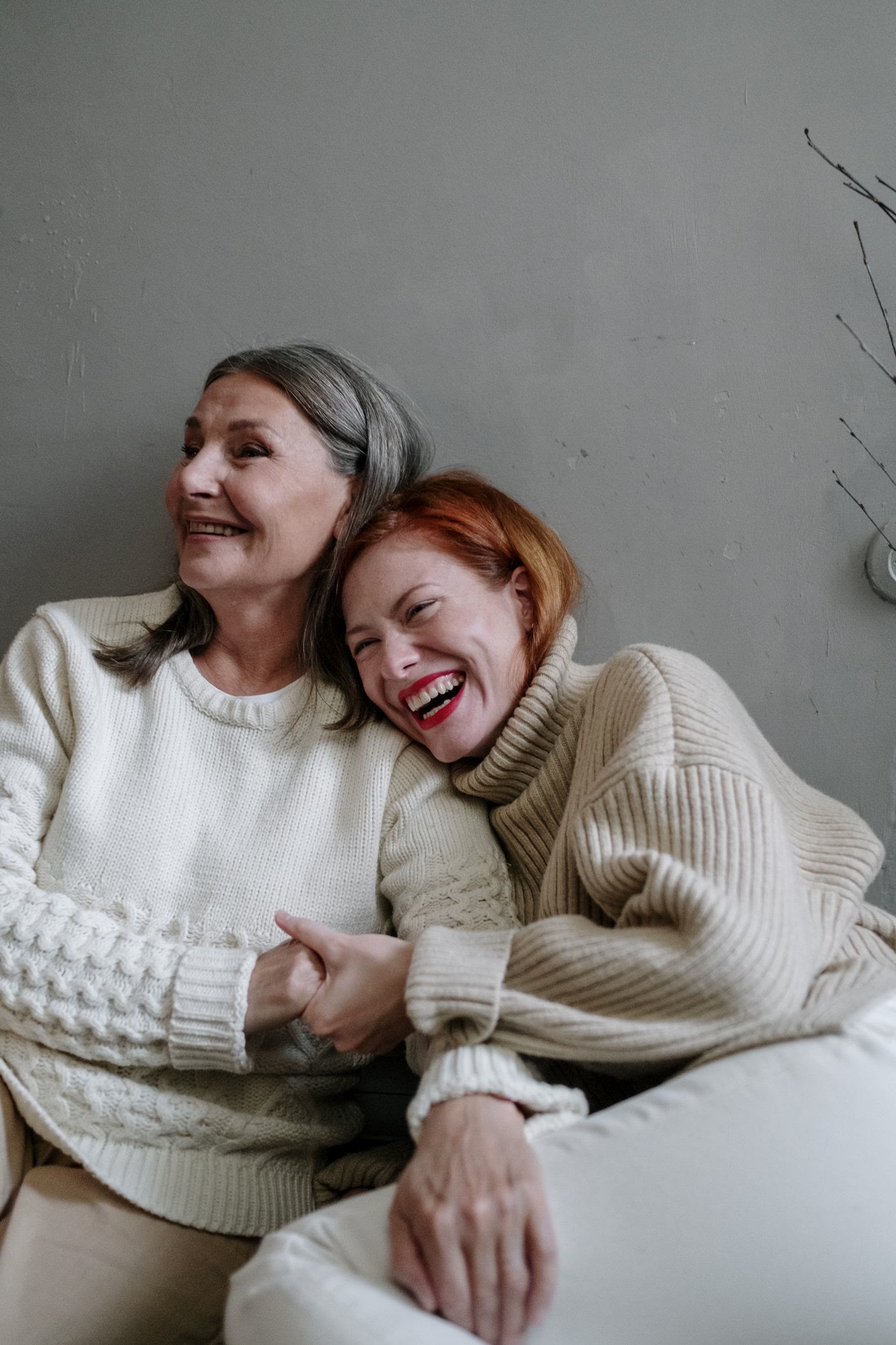 A mother and her adult daughter laughing together in jumpers