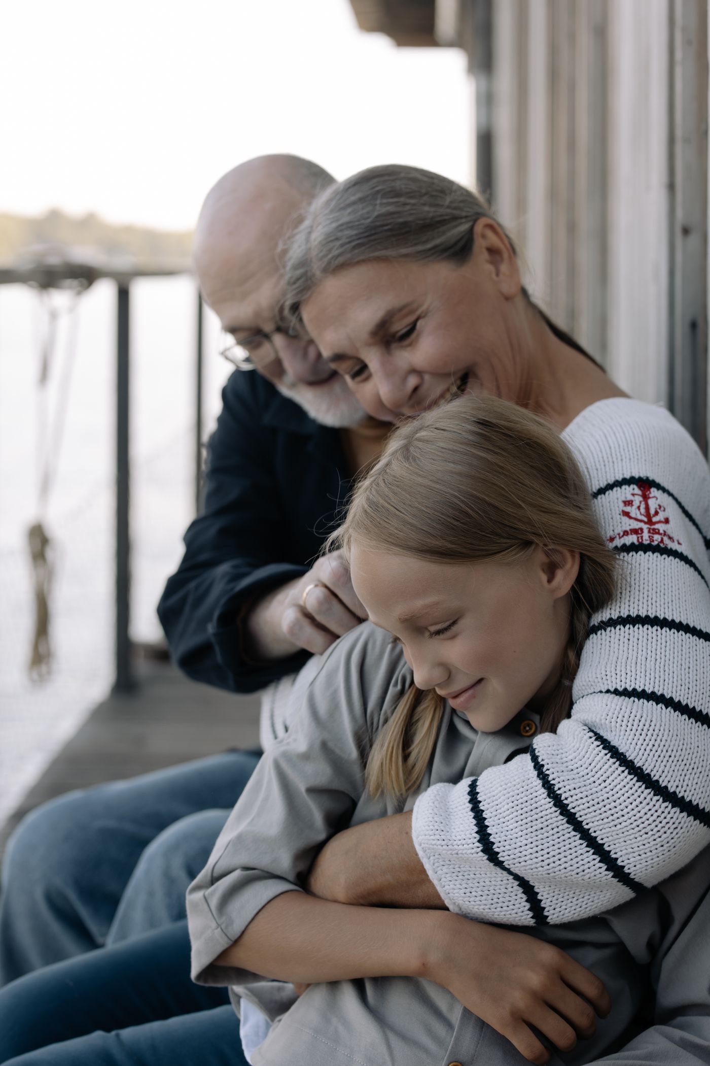 Grandparents hugging their grandchild on a jetty in summer