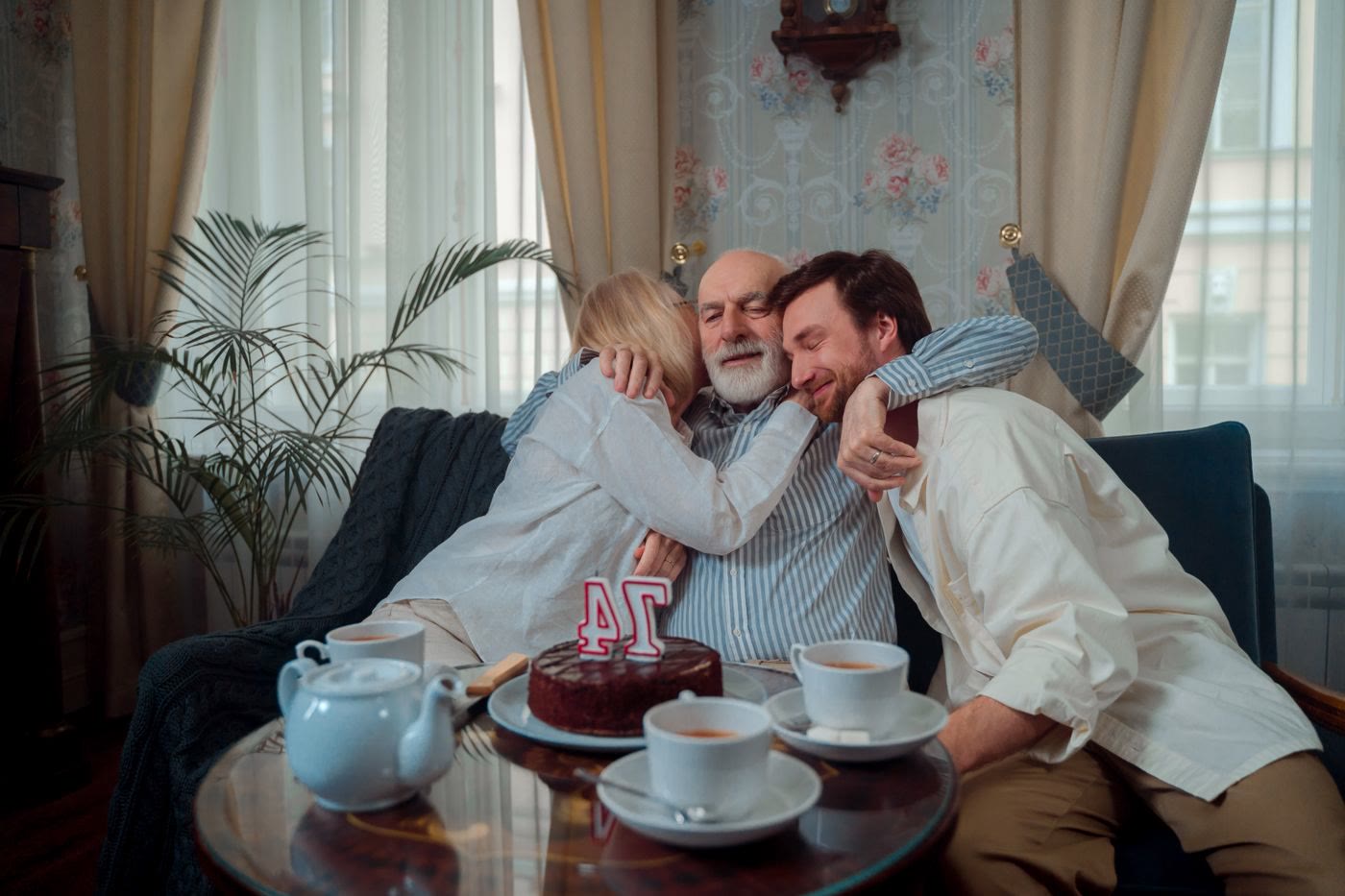 Adult children hugging their father at his birthday, the cake reads 74